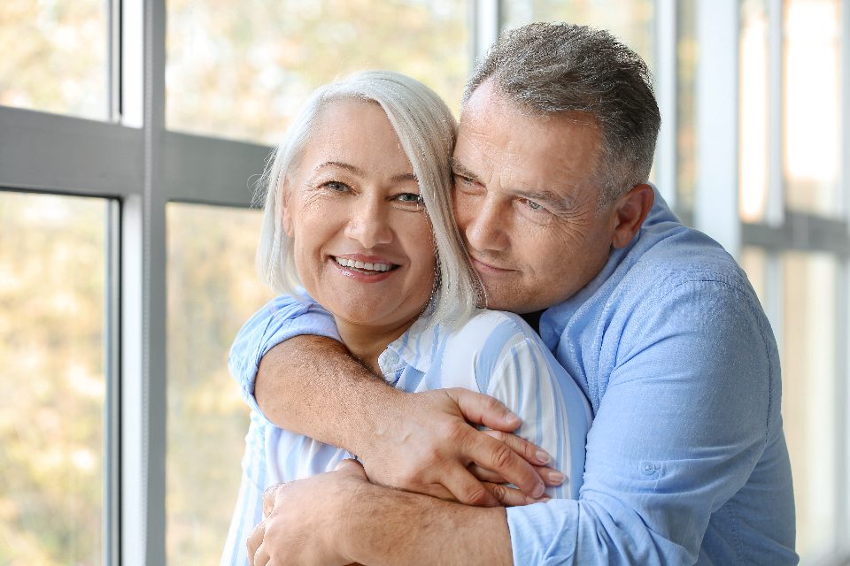 Couple in their sixties embracing by a window